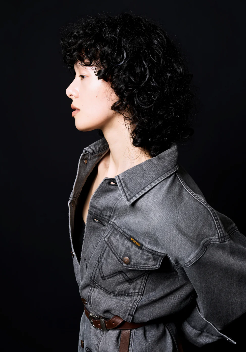 Whim Gazette × Wrangler ブラックのブロークンツイルデニムジャケットを着たモデルの横顔